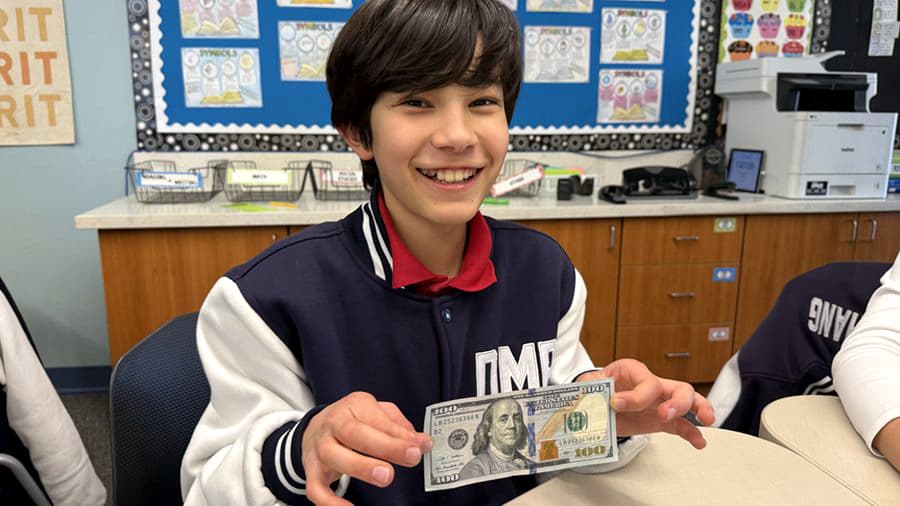 A sixth grader proudly holds up a prop bill during a class activity