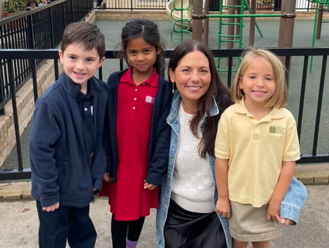 Kindergarteners smiling with their teacher on the playground