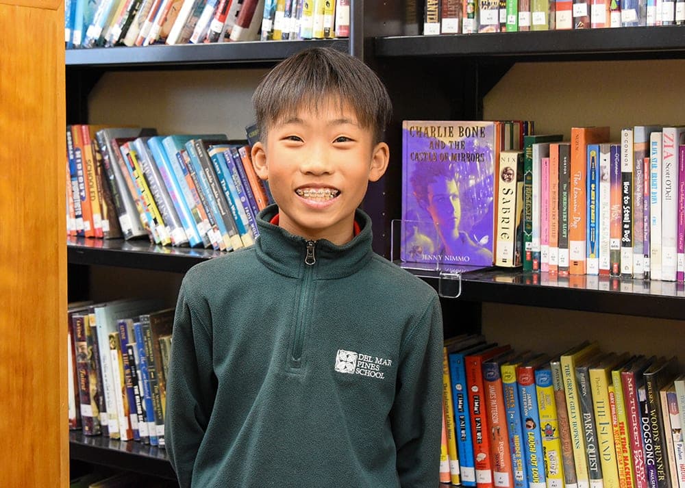 A student in the school library in front of the shelves