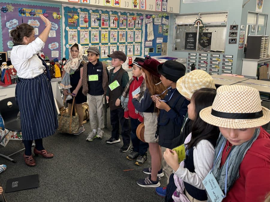 A teacher in period costume leads students dressed as immigrants through a living-history lesson