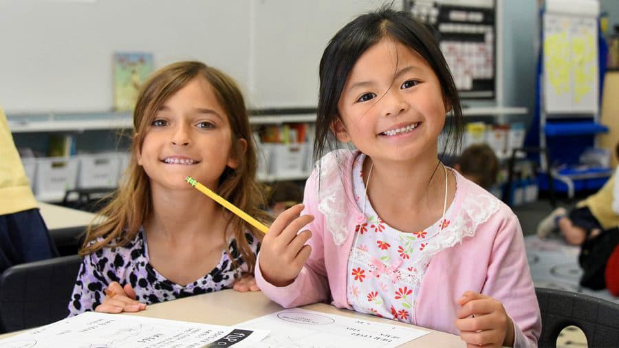 Two girls smiling over their classwork