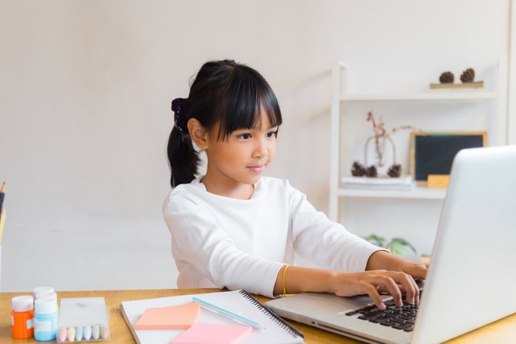 Young girl typing on a white laptop.