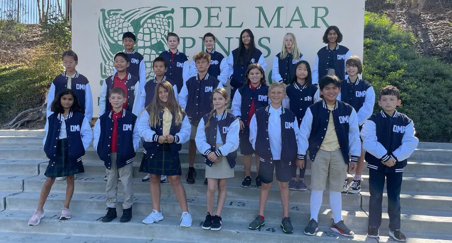A group of Del Mar Pines students stand together on outdoor steps. The students are posing for a group photo, smiling or looking at the camera.